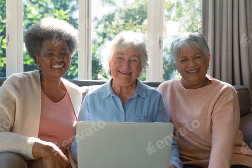Preview: Three happy diverse senior woman sitting on sofa and using laptop