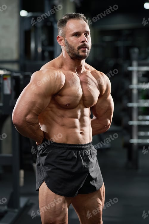 Preview: Attractive bodybuilder performing strong body in sport gym.