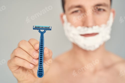 Preview: Smiling young man holding razor blade in hand