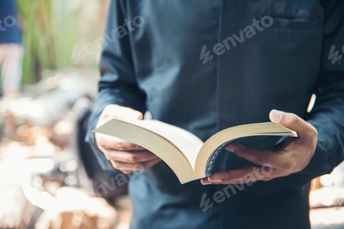 Preview: Asian man holding book reading magazine at green park in natural garden