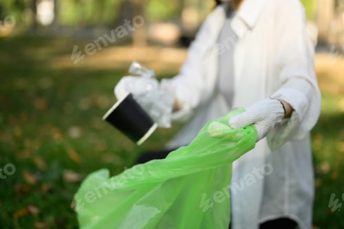 Preview: Young woman in gloves collecting garbage in the park. Environmental responsibility concept