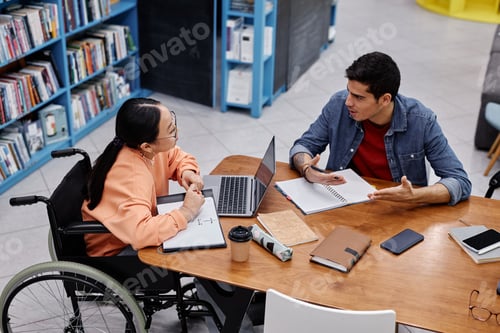 Preview: Asian teenage girl with disability talking to friend in college library