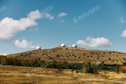 Preview: Three towering antennas overlooking a serene landscape of rolling hills and lush grass in a remote