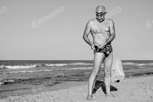 Preview: Sport swimmer senior man training to swim open water with beach on background - Black and white edit
