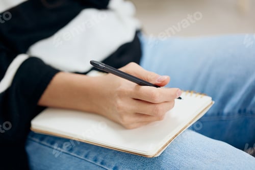 Preview: Hand of woman in striped sweatshirt writes in craft notebook with pen. Closeup, details. Banner