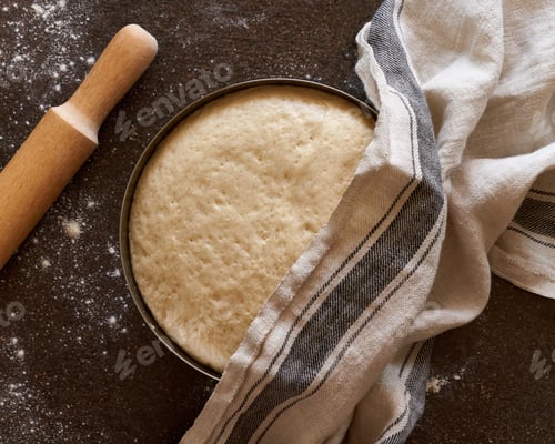 Preview: Raw yeast dough resting and rising in large metal bowl with linen towel