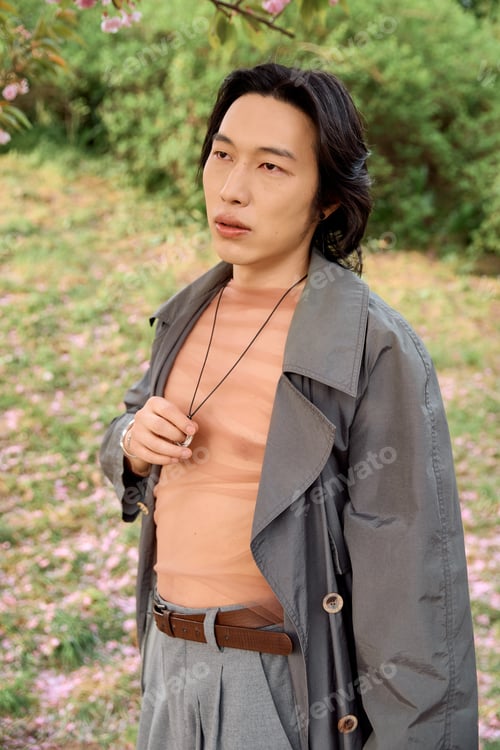 Preview: Stylish young man in grey outfit poses confidently in a blooming park setting