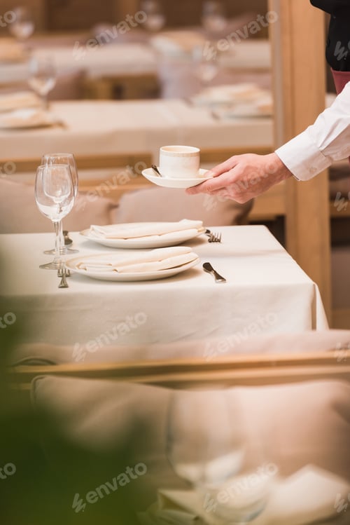 Preview: Cropped image of waiter serving cup of coffee on a table