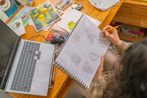 Preview: Graphic designer drawing sketches in home studio with laptop
