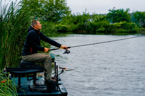 Preview: Fisherman casts a fishing rod or spinning rod into the water while sitting on river bank on pier
