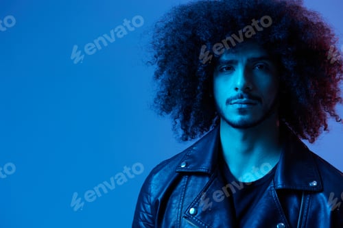 Preview: Portrait of fashion man with curly hair on blue background multinational, colored light, black