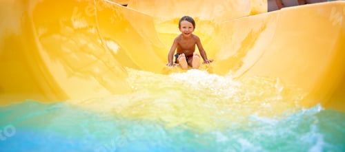 Preview: Cheerful blue-eyed kid on a water slide in the water park, a little boy merrily slides into the