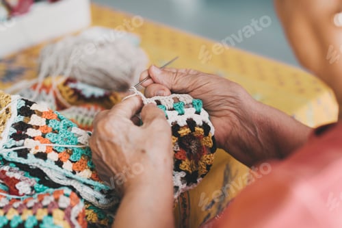 Preview: Close up of old female hands doing knit work with wool at home for indoor leisure activity. Aged ret