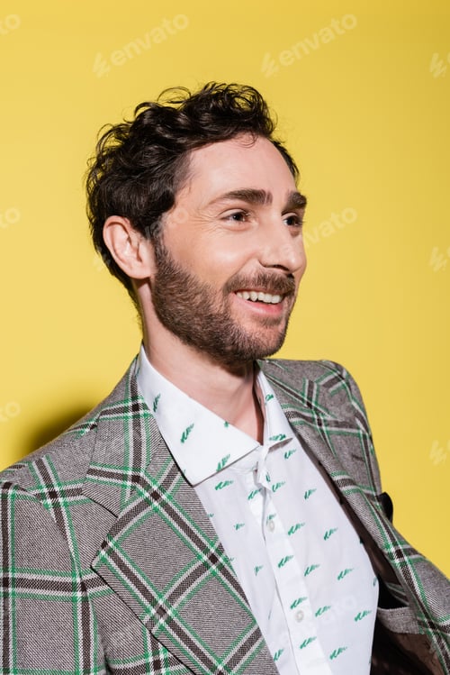 Preview: Portrait of smiling bearded man in shirt and jacket looking away on yellow background