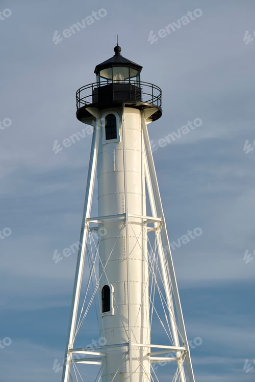 Preview: White tall lighthouse on sea shore against blue sky for commercial vessels navigation