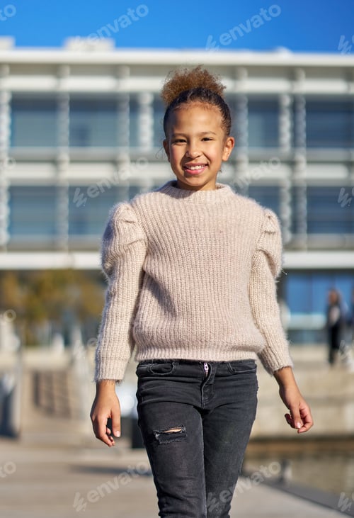 Preview: A young girl wearing a sweater and jeans walks past a building