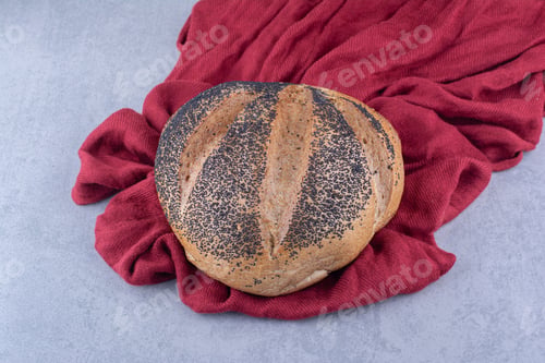 Preview: Piece of cloth under a loaf of black sesame coated bread on marble background