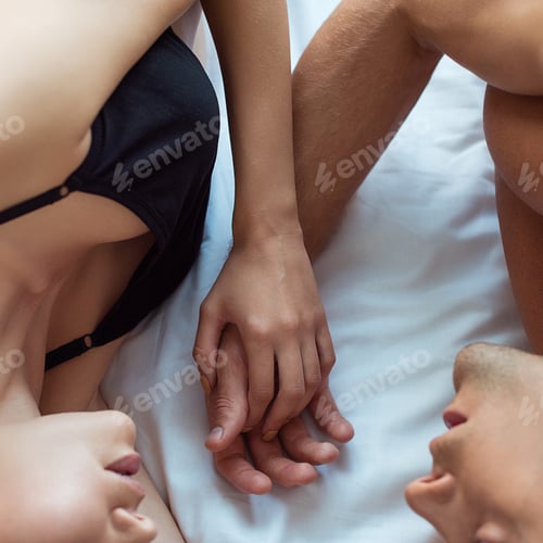 Preview: cropped view of man and young woman holding hands while lying on bed