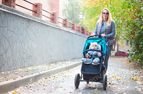 Preview: Young blond woman with stroller going for a walk in a park