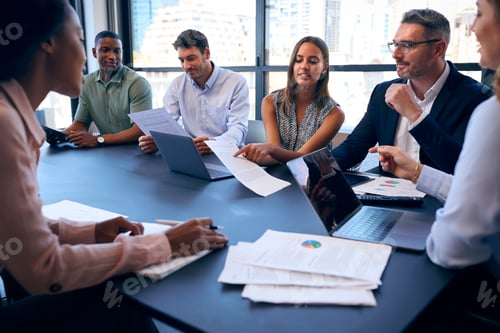 Preview: Multi-Cultural Business Team Meeting Around Office Boardroom Table With Laptops Discussing Documents
