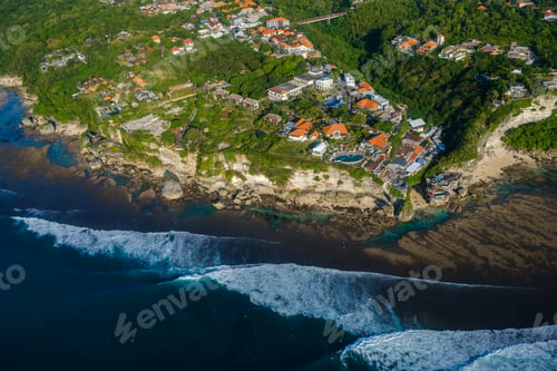Preview: Aerial View of Coastal Town with Lush Greenery and Waves Crashing on Rocky Shore