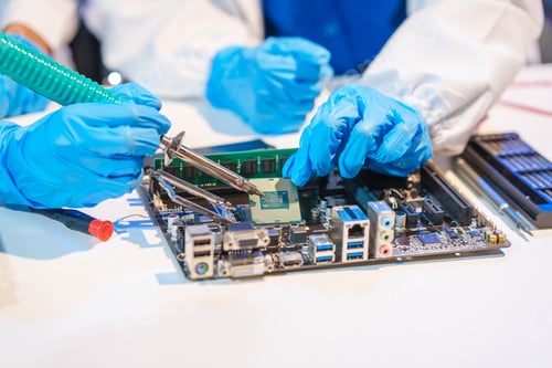 Preview: Close-up of a technician wearing gloves soldering electronic components at a desk in an office