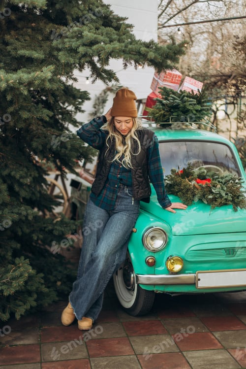 Preview: Young blonde woman near retro car with Christmas decorations