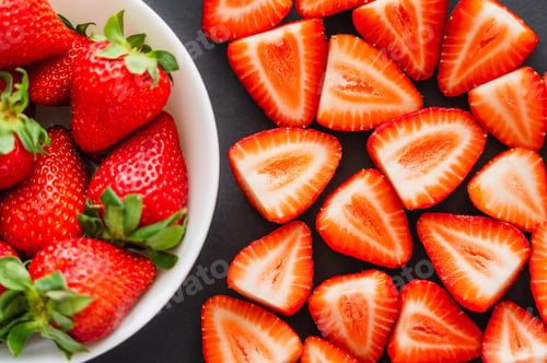 Vista previa: Flat lay with cut and whole strawberries in bowl on black background