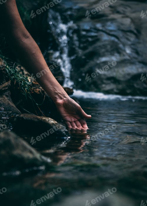Preview: Hand Touches Water Near Waterfall in Nature