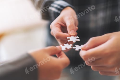 Preview: Closeup image of many people hands holding and putting a piece of white jigsaw puzzle together