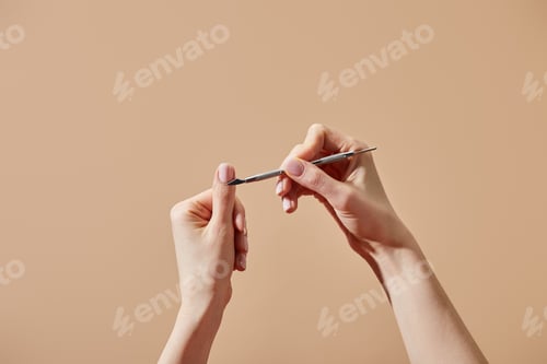 Preview: Cropped view of woman doing manicure using cuticle pusher isolated on beige