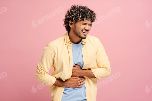 Preview: Sick Indian man suffering from strong stomach ache on pink background