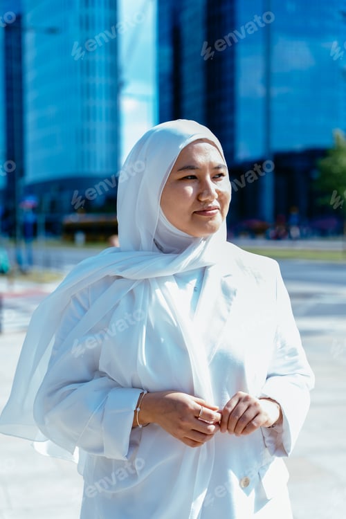 Preview: Muslim woman in white hijab looking aside on sunny street