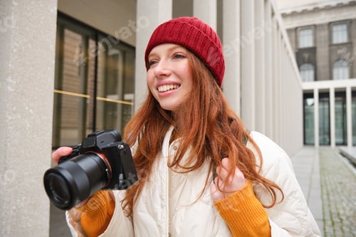 Preview: Smiling redhead girl photographer, taking pictures in city, makes photos outdoors on professional