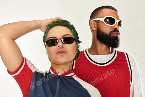 Preview: Stylish multicultural couple in trendy sunglasses poses under studio lights