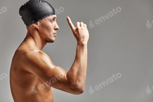Preview: Young professional swimmer man indicates with fingers up showing a blank space.