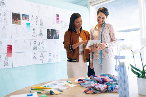 Preview: Happy diverse female fashion designers discussing over digital tablet