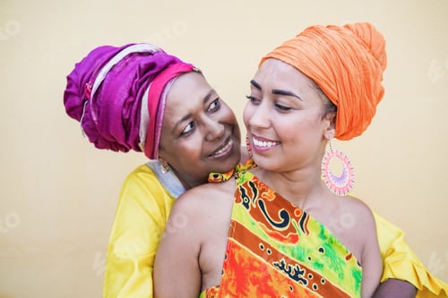 Preview: Happy african mother and adult daughter hugging each other outdoor while wearing traditional dress