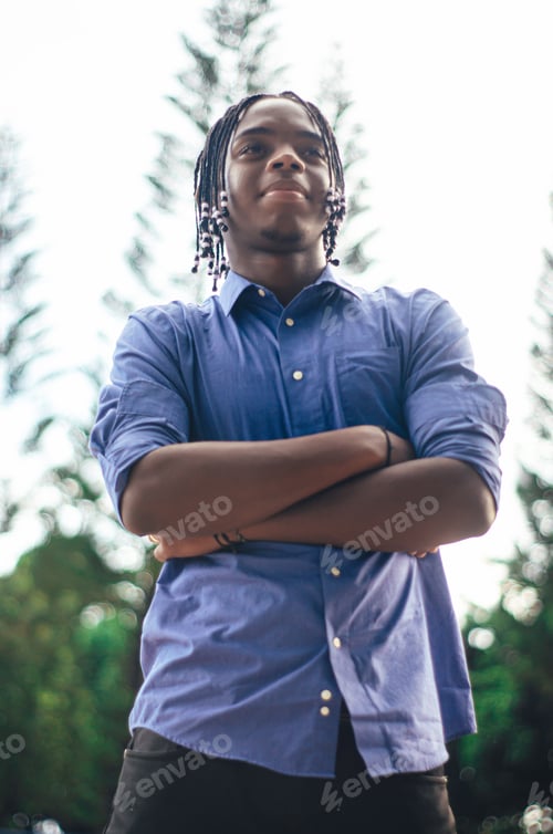 Preview: young latino dominican man with dark skin and curly and braided hair in the park with blue shirt