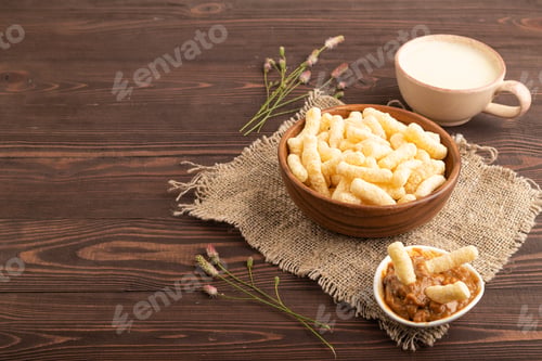 Preview: Corn flakes sticks with caramel in wooden bowl on brown wooden, Side view, copy space.