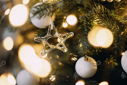 Preview: Modern glass christmas ornaments, wooden garland, white baubles and golden christmas lights close up