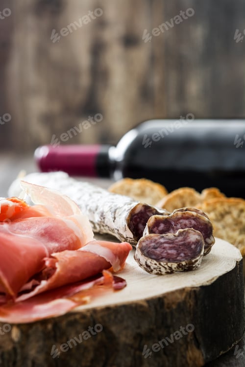Preview: Sliced sausage, prosciutto and red wine bottle resting on wooden board