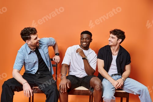 Preview: jolly diverse men in casual street outfits smiling happily on orange backdrop, fashion concept