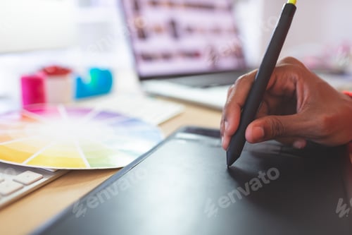 Preview: Close-up of young mixed-race female graphic designer using graphic tablet at desk