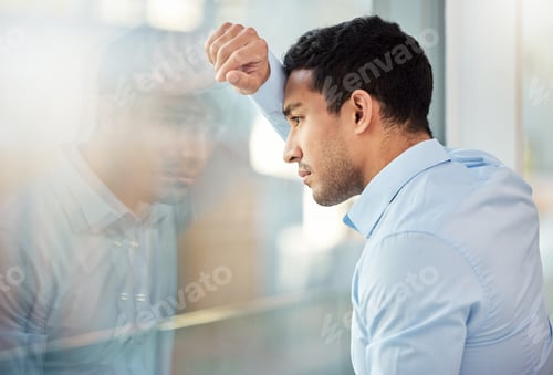Preview: Shot of a young businessman leaning against a window looking depressed
