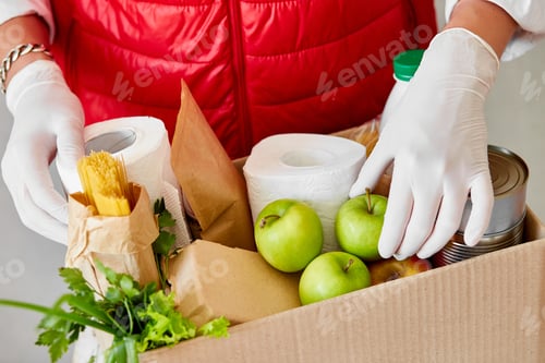 Preview: Volunteer in the protective medical mask and gloves putting food In donation box.