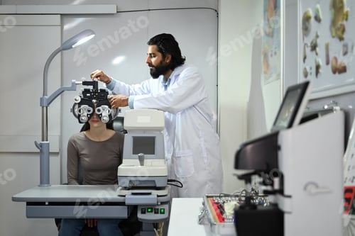 Preview: Male ophthalmologist with beard in white coat checking eye vision of patient .