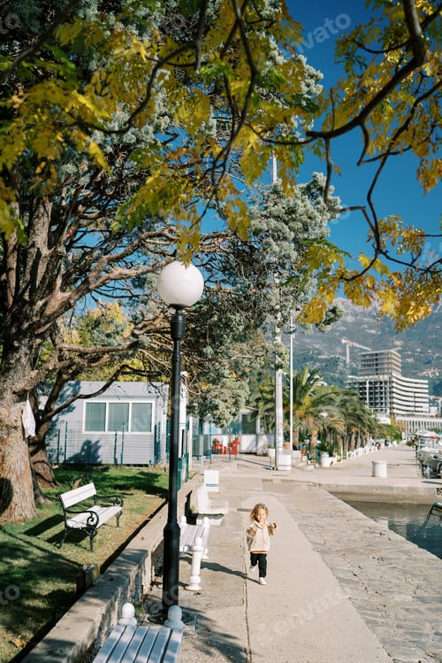 Preview: Little girl runs along the sunny embankment past wooden benches