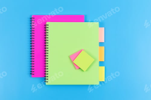 Preview: Green and magenta copybooks and sticky notes on blue background, top view.