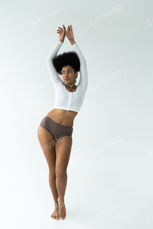 Preview: full length of barefoot african american woman posing in long sleeve shirt and panties on white